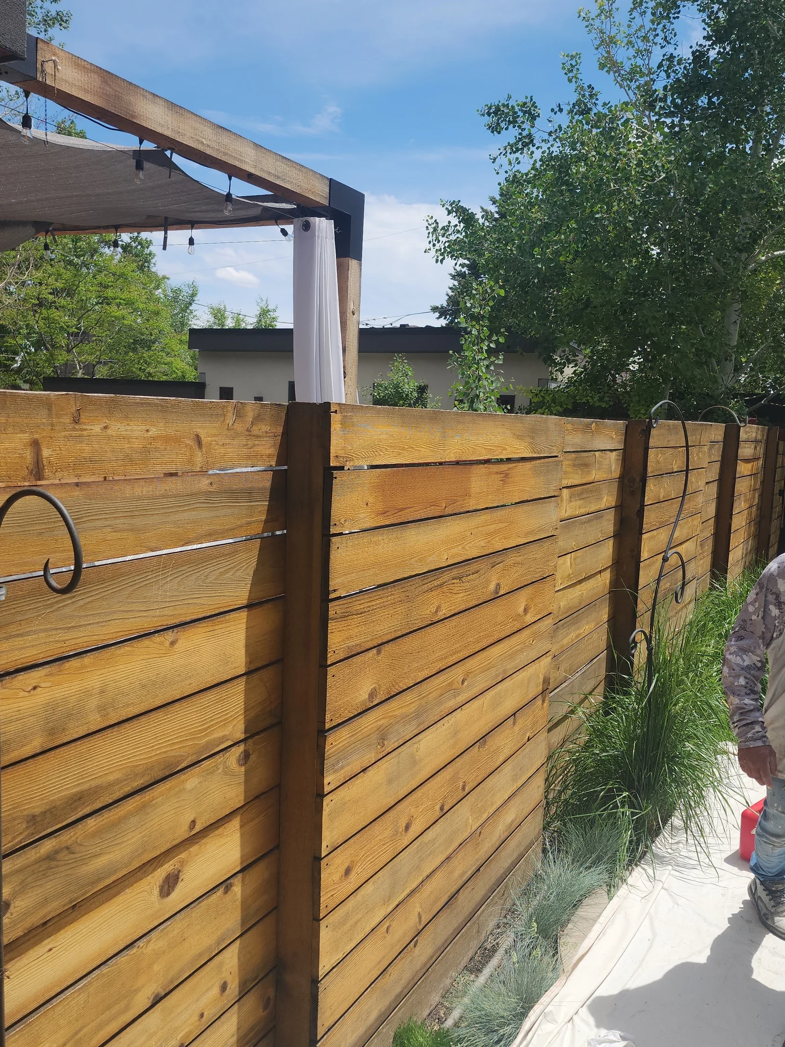 Horizontal wood fence with steel cable railings and dark posts, pergola overhead