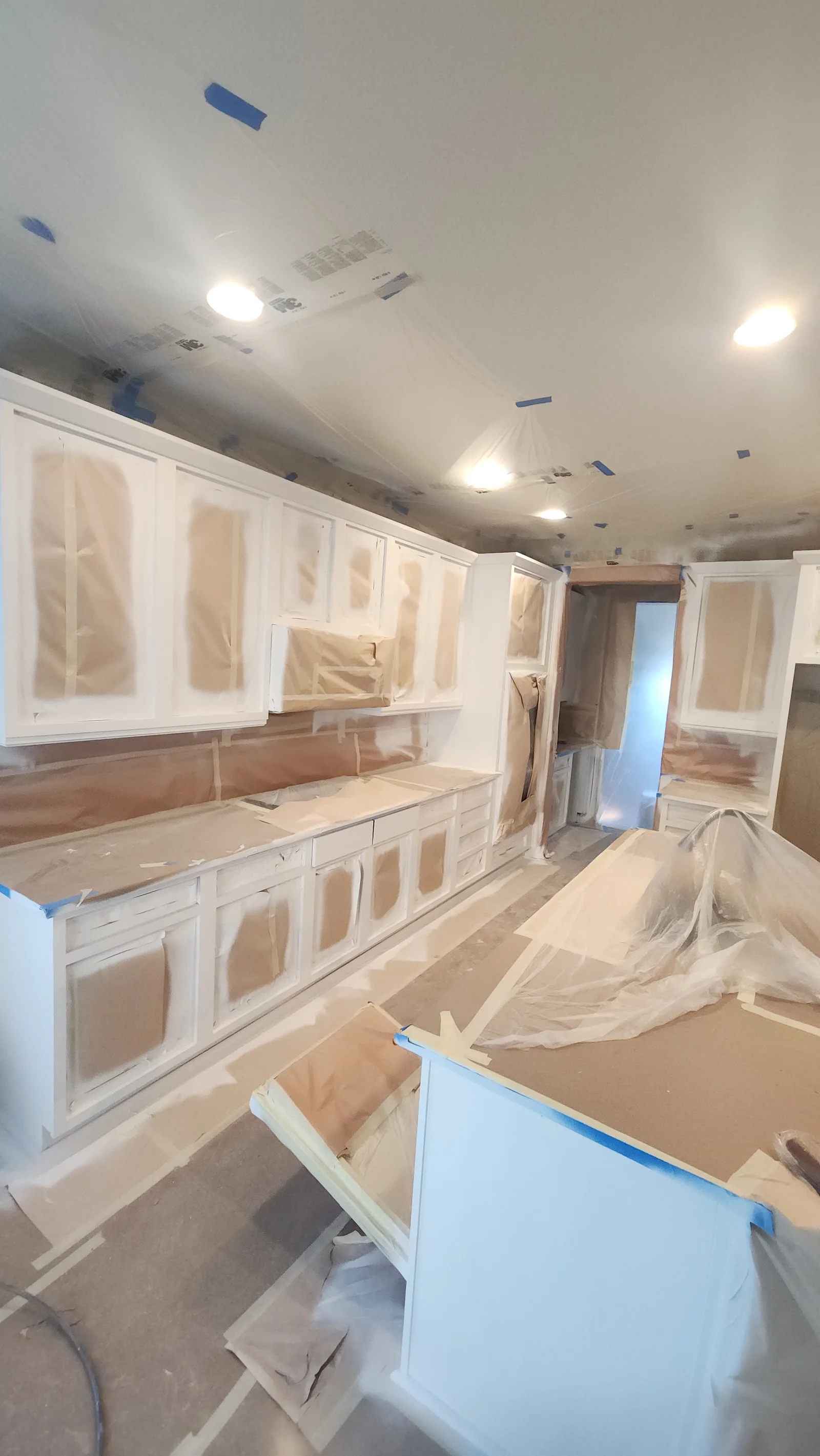 White painted kitchen cabinets with plastic protection, recessed lighting, and drywall ceiling prep